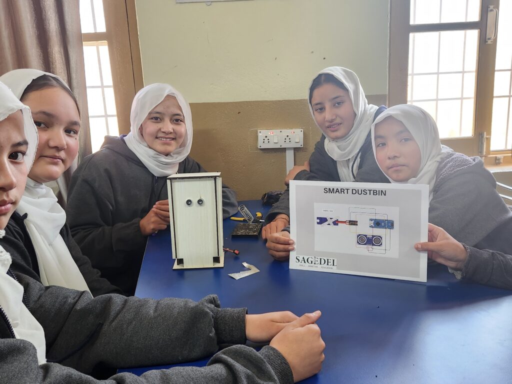 Group of students in a classroom proudly displaying a Sagedel Smart Dustbin robotics project and its circuit diagram featuring an Arduino and ultrasonic sensor